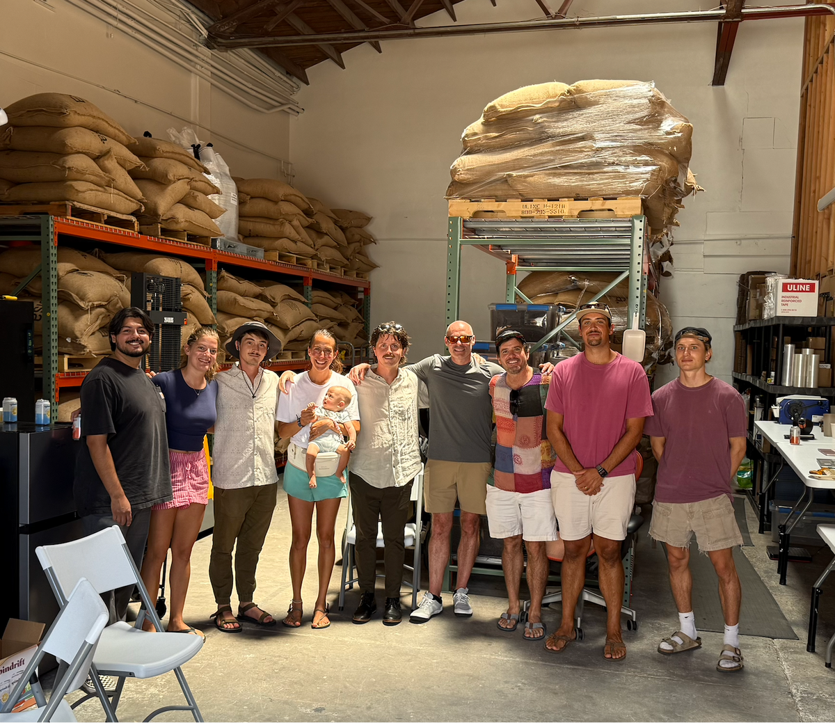 Excelsa team in front of stacked green coffee bags in our San Diego warehouse